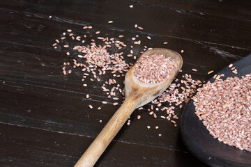 Grains of rice scattered on a table with grain in a wooden spoon and another portion inside a black...