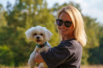 Portrait of smiling young woman kiss dog in Natural Park. Dog lover woman wearing blue dress with dog during good day. Concept of friendship and beautiful girl with a small dog