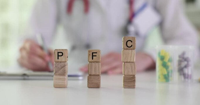 Abbreviation PFC made from wooden cubes against doctor with stethoscope in hospital. Woman medic in uniform prescribes medication to patient