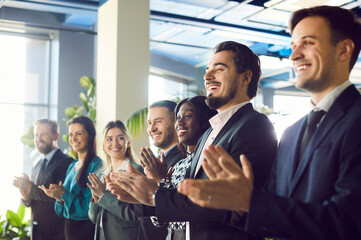 Obraz premium Group of happy multiethnic satisfied audience applauding to speaker after business training or conference. Diverse satisfied male and female businesspeople standing in a row and clapping their hands.
