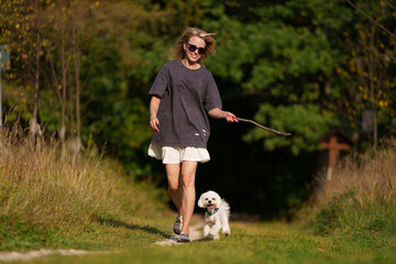 Girl throws a stick to the dog in natural park of Town. Woman in blue dress walking with dog