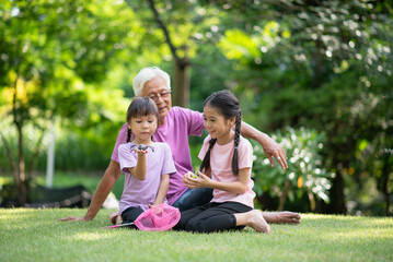 Fototapeta premium Happy Asian family children having fun and catches a net of insects with her grandfather in the park