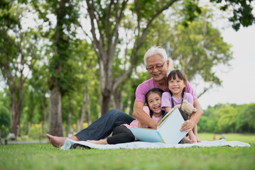 Fototapeta premium Happy Asian family children reading a book with her grandfather