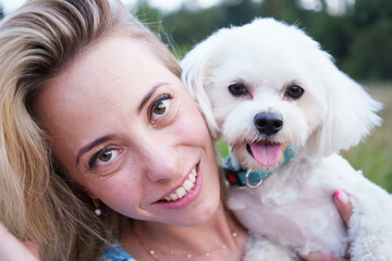 Portrait of smiling young woman kiss dog in Natural Park. Dog lover woman wearing blue dress with dog during good day. Concept of friendship and beautiful girl with a small dog