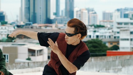 Motion shot of B-boy dance performance by professional street dancer at rooftop with sky scrapper, city view. Attractive asian hipster show energetic footstep. Outdoor sport 2024. Closeup. Hiphop.