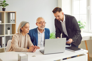 Smiling happy elderly couple talking with man advisor about health insurance or investments sitting...