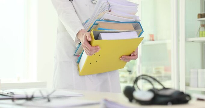 Woman doctor carries stack of ring binders putting on table in hospital. Female medic in uniform prepares for boring paperwork slow motion