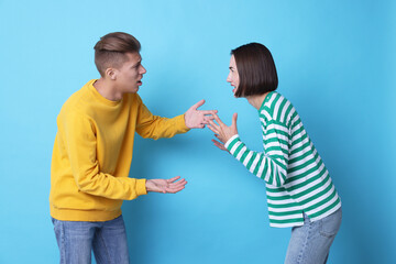 Obraz premium Emotional young couple having quarrel on light blue background