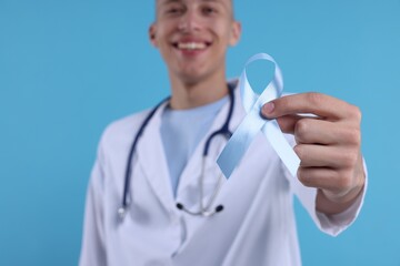 Prostate cancer awareness. Doctor holding light blue ribbon as symbol of support on color...