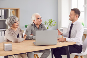 Smiling happy elderly couple talking with man advisor about health insurance or investments sitting...