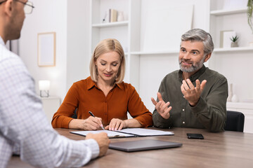 Pension plan. Couple consulting with insurance agent at table indoors