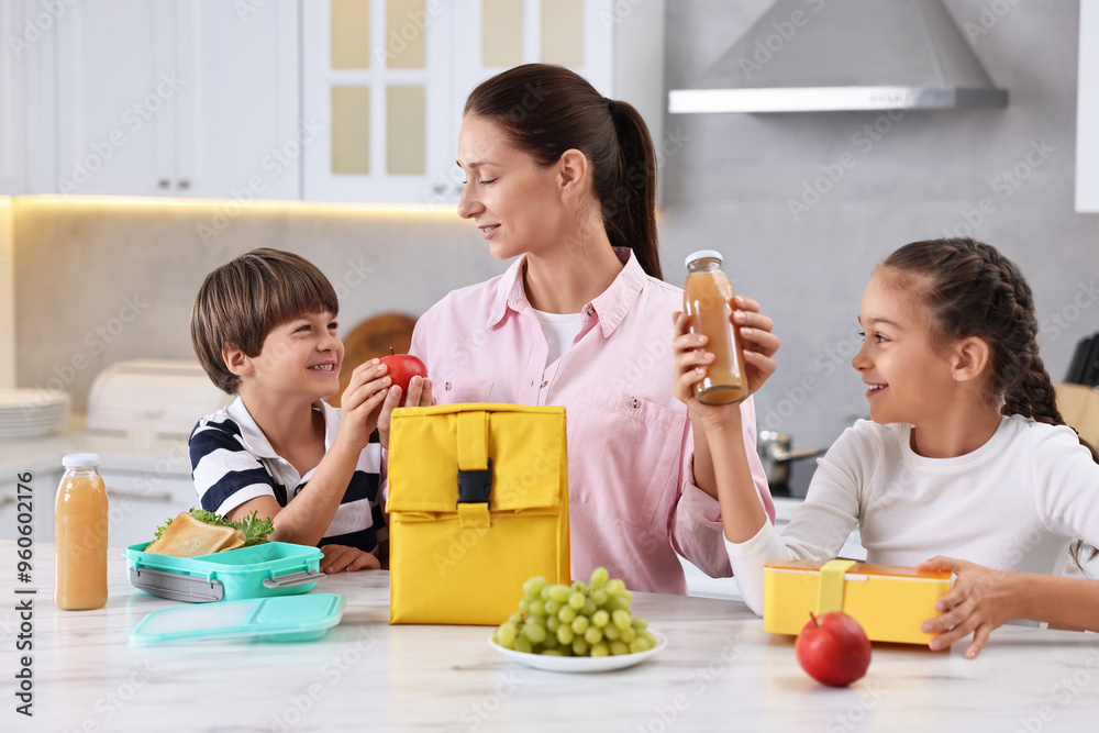 Poster Mother and her children preparing school lunch boxes with healthy food at table in kitchen