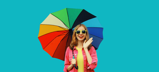 Stylish happy smiling young woman holding colorful umbrella, cheerful girl on bright blue background