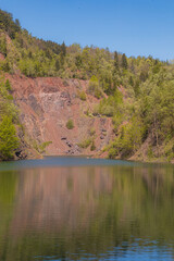 Peaceful forest Kamyki lake after old quarry reflecting the vibrant green foliage under a clear blue sky, creating a serene and tranquil atmosphere © Pawel-Wierzchowski