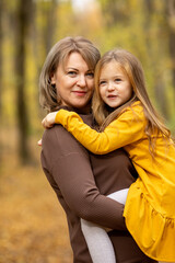 Fototapeta premium Beautiful mother and daughter walking in the park in autumn, portrait. Mom and daughter, family concept. A little girl in her mother's arms. Happy family on an autumn walk