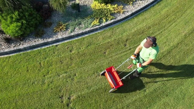 Lawn Care Expert Using a Spreader to Fertilize Grass in a Well-Maintained Garden