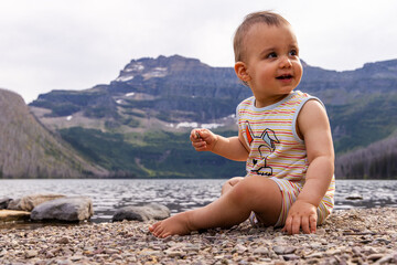 Fototapeta premium Adorable Baby Sitting by a Serene Lake in Waterton, Alberta, Canada with Scenic Mountain View