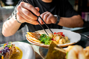 Close-up of a gourmet dish featuring prawns, cherry tomatoes, and herbs, elegantly presented and being picked up with chopsticks. Perfect for culinary, food photography, and gourmet dining themes.