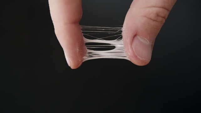 Fingers covered in a sticky white slime. Isolated male hand separates fingers stretching the sticky goo strands.