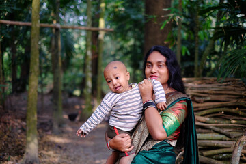 Fototapeta premium South asian young lady with a traditional costumes holding her baby boy in a garden 