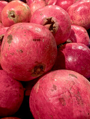 Fresh red pomegranates piled together in a vibrant display at a local market during autumn harvest season. Background vertical.