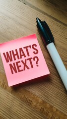 Wooden table with pink sticky note WHATS NEXT?, black marker beside Vertical Mobile Wallpaper