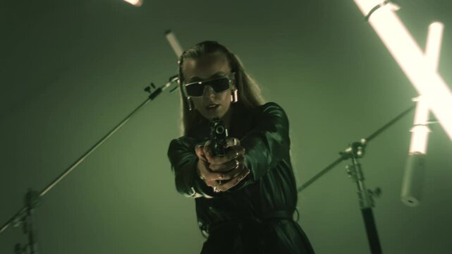 Dangerous female hitman aiming with a handgun in a dark room
