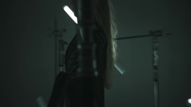 Female agent walking in a leather coat holding an m9 handgun in a dark room lit by led lamps
