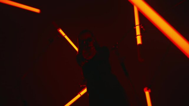 Beautiful badass lady agent in leather coat and sunglasses aiming a gun in a dark room with red tube lights