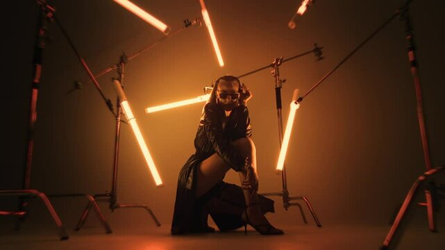 Mysterious woman in a leather coat and high heels surrounded by LED tube lights in a dark room