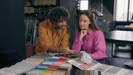 Multiracial couple clients customers looking textile samples discuss design ideas Arabian Indian man salesman Caucasian woman buyer choosing fabrics color for fashion clothes dressmaking in atelier