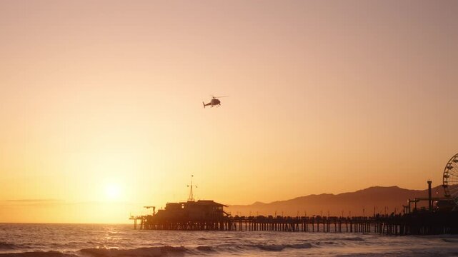 LAPD helicopter flying over Santa Monica pier during a scenic sunset in Los Angeles, California, USA