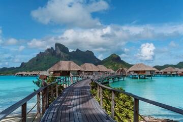 View of the Mount Otemanu through turquoise lagoon, palm trees and overwater bungalows on Bora Bora...