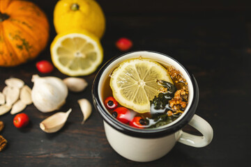 Virus protection, cold and flu prevention, natural immune boost remedies, cup of herbal tea, lemon, garlic, pumpkin seeds, ginger and dog rose fruit on a dark wooden background