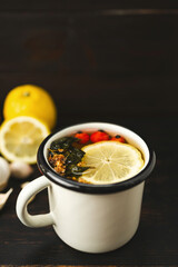 Virus protection, cold and flu prevention, natural immune boost remedies, cup of herbal tea, lemon and dog rose fruit on a dark wooden background