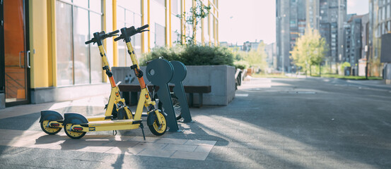 Electric scooter for rent on the street. Two bright scooters are parked on the sidewalk on a city street © Anna