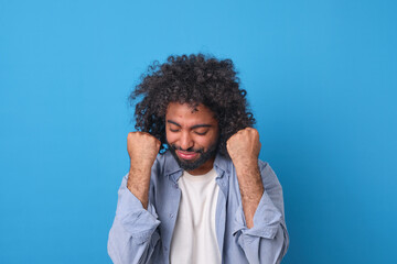 A young man with curly hair expresses pure joy, raising his fists in delight. His radiant smile...