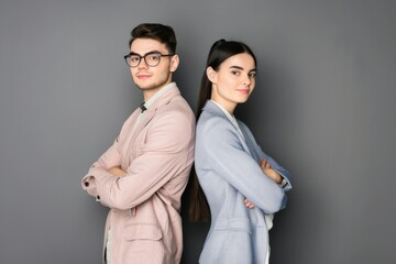 Dynamic business partnership represented by young professionals standing confidently back-to-back in neutral attire against a grey backdrop