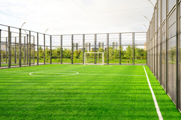 An empty bright green outdoor soccer field with artificial turf, fenced with a metal fence, for...