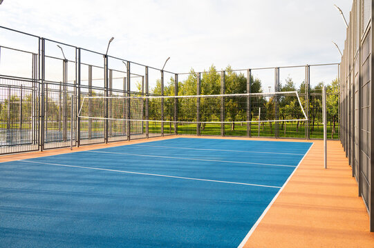 An outdoor volleyball court with a blue surface and a metal fence in the city park