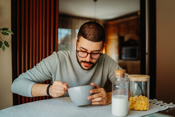 Young caucasian man eating corn flakes for breakfast at home