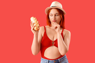 Thoughtful young woman with hot dog on red background
