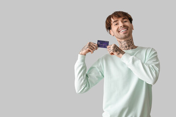 Tattooed young man with credit card on light background