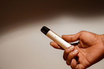 hand holding an e-cigarette on a black background with empty photocopy space.