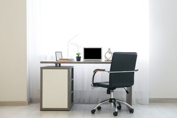 Stylish workplace with modern laptop, books, decor and lamp near window in light office