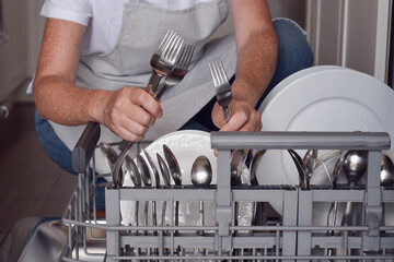 Woman is unloading cutlery from a dishwasher in a kitchen