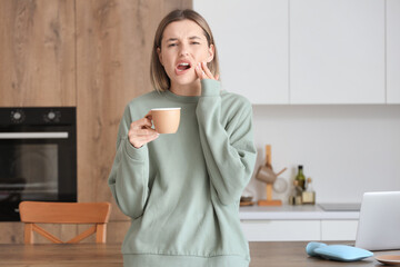 Young woman with cup of hot coffee suffering from tooth ache at home