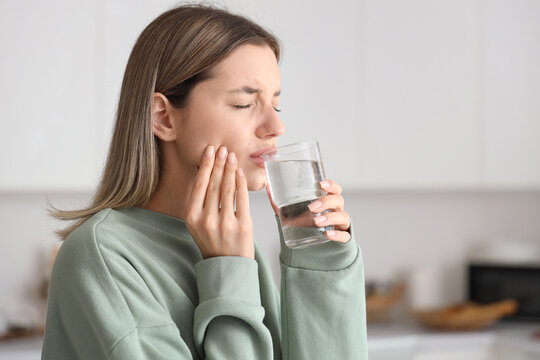 Young woman with glass of cold water suffering from tooth ache at home