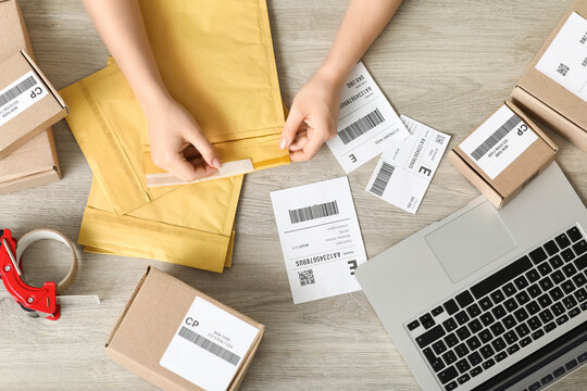 Female postal worker with packages and labels on table, top view