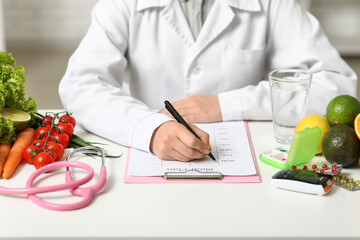 Young female nutritionist with healthy food, glass of water and stethoscope writing diet plan in...